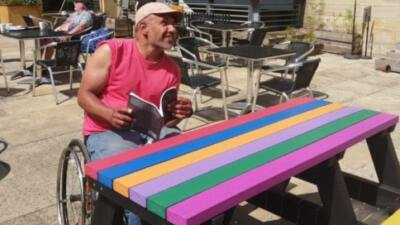 A wheelchair user sitting at a multicoloured Bradshaw recycled plastic picnic table on the cafe terrace at Hebden Bridge Town Hall