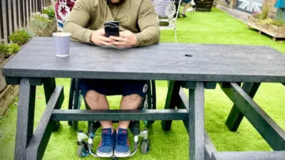 Man on wheelchair using mobile phone sat at Bradshaw British Recycled Plastic Picnic Table .