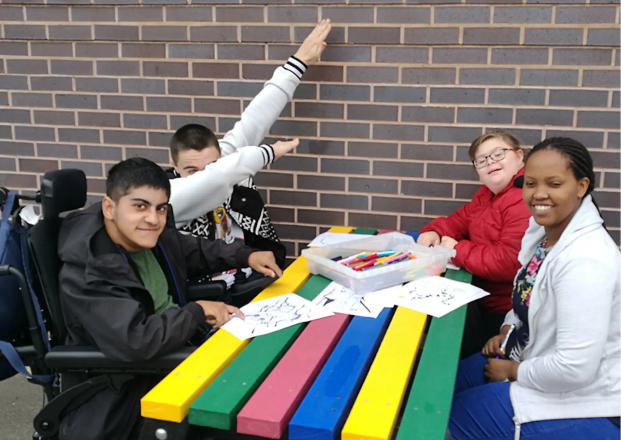 xr:d:DAFU2PiqN-8:2,j:43718415606,t:22121516 Young people drawing, smiling, laughing at colourful table. Includes wheelchair users. British Recycled Plastic