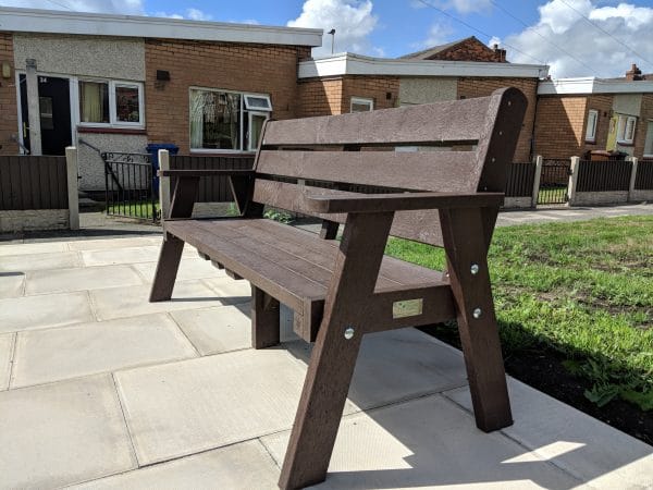 A brown recycled plastic Ilkley sloper bench with arms on a housing estate