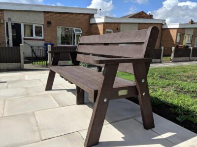 A brown recycled plastic Ilkley sloper bench with arms on a housing estate