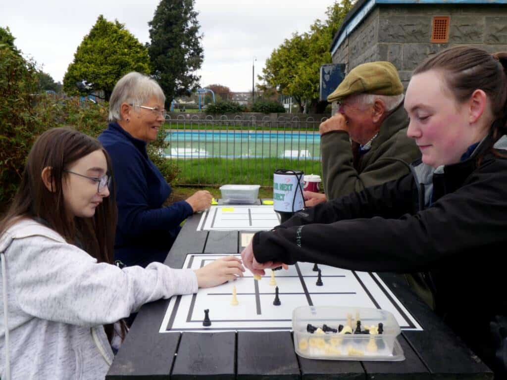 People playing noughts and crosses outdoors at an otley picnic table