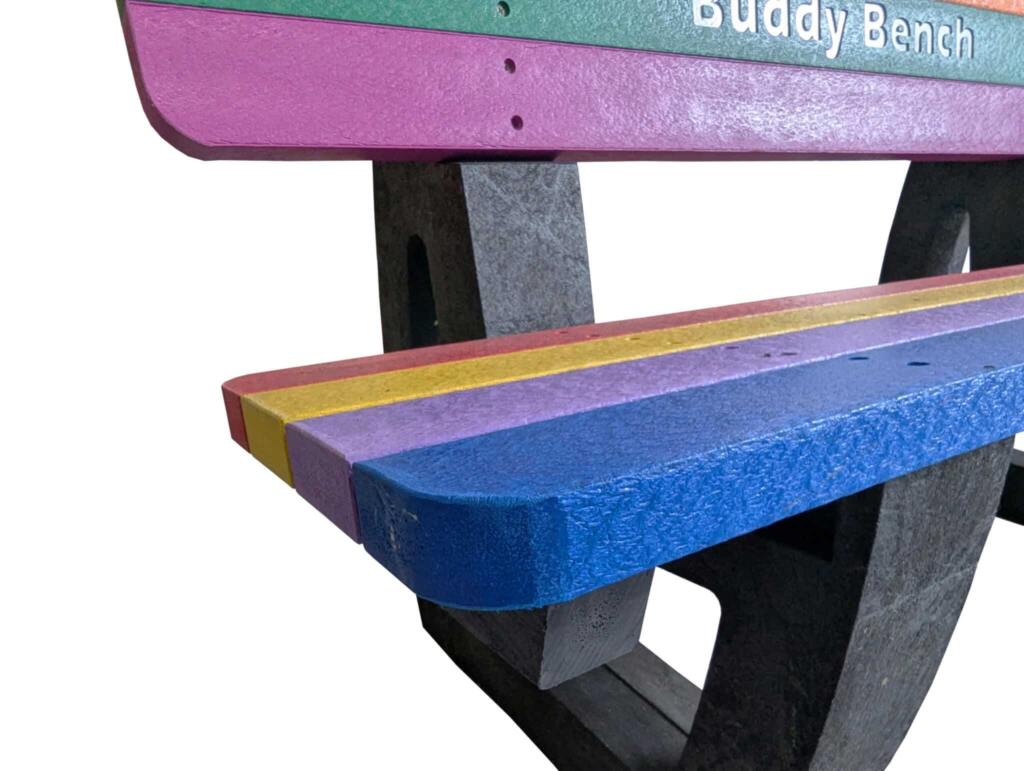 A bright, welcoming Buddy Bench made from recycled plastic, placed in a school playground to encourage children to sit, talk, and make new friends