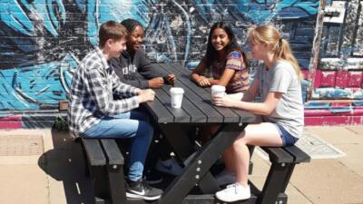 Four teenagers seated at a British Recycled Plastic Batley Walkthrough Picnic Table .