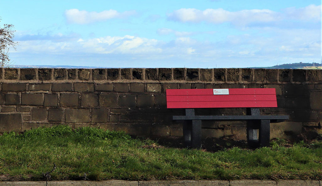 A red and black recycled plastic Harewood bench produced as part of a series to commemorate the Sowood Poppy Trail near Halifax in West Yorkshire