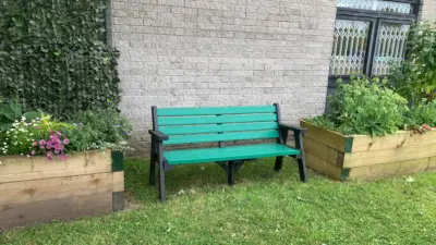 Green Ilkley sloper bench beside wooden planters. British Recycled Plastic