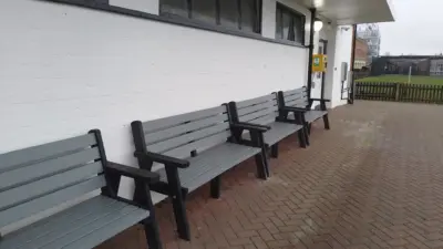 Row of grey wooden benches outside a school. British-Recycled-Plastic-