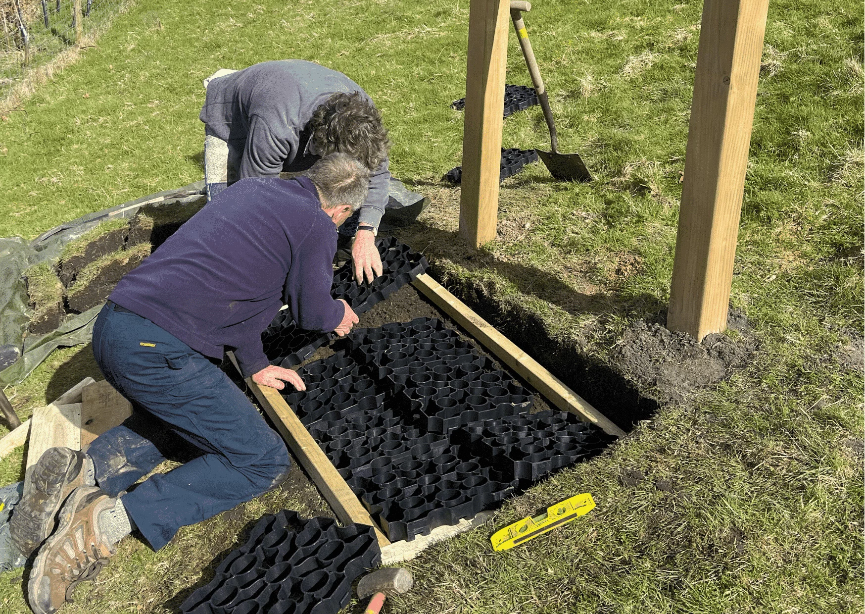 people laying ground reinforcement grids down into some grass 