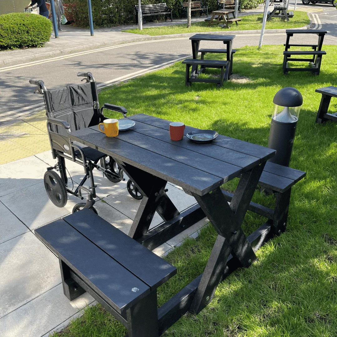 Wheelchair-accessible black recycled plastic picnic tables, set on grass near a paved path.