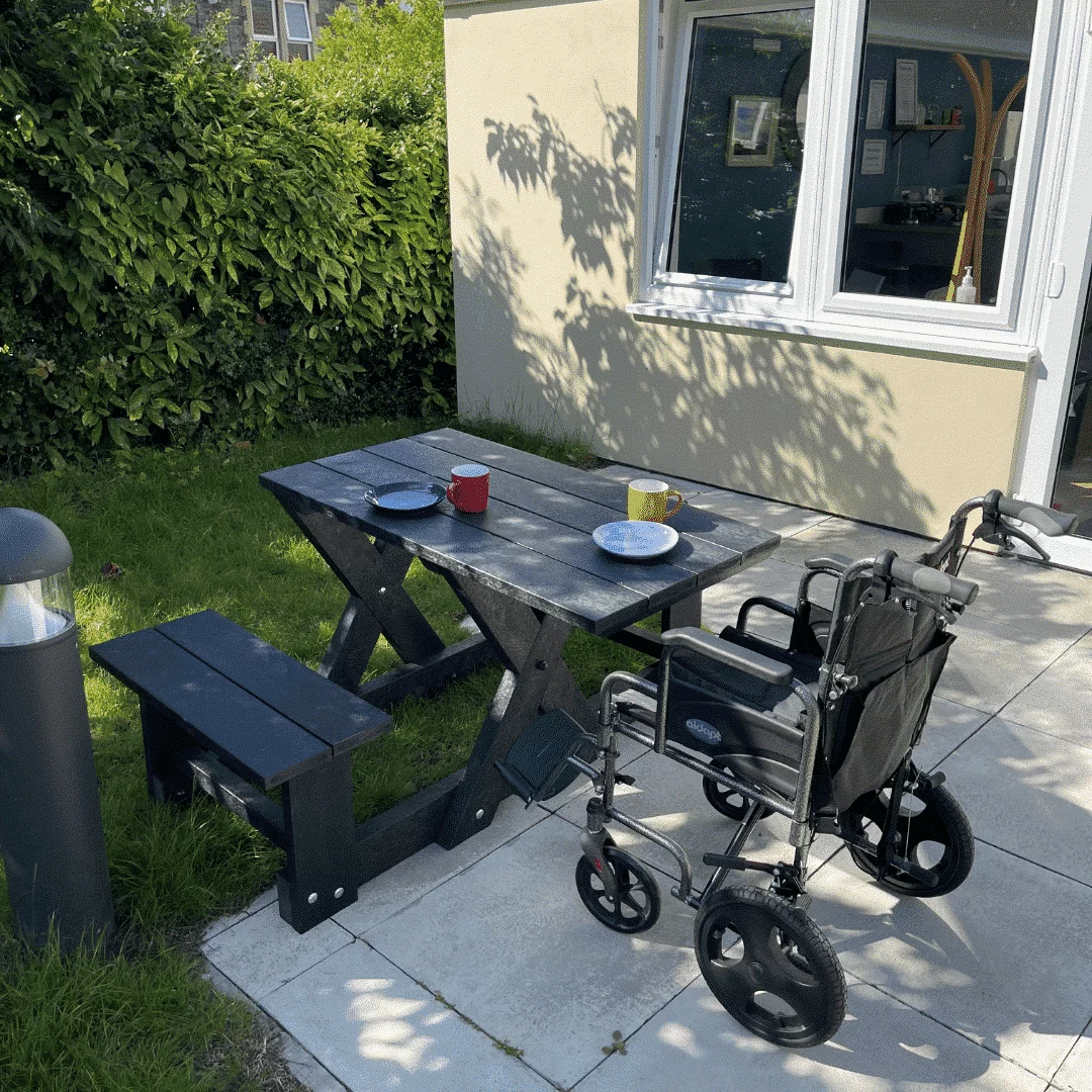 Two seater compact picnic table in a sunny outdoor space with wheelchair positioned to the side.