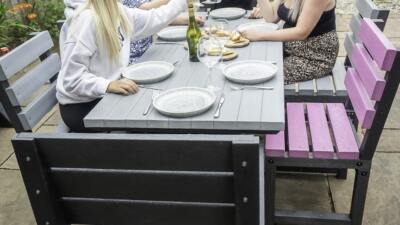 Black Birchcliffe dining set made from weather-resistant recycled plastic, situated in a garden with a family enjoying wine around the table.