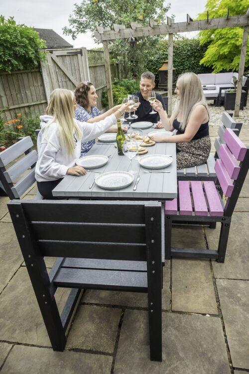 Black Birchcliffe dining set made from weather-resistant recycled plastic, situated in a garden with a family enjoying wine around the table.