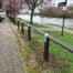 Recycled plastic bird's mouth fencing installed along a riverside path, with a river, trees, and a footpath visible in the background.