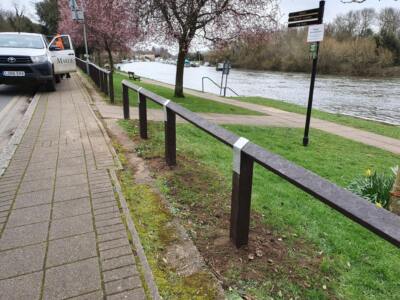 Recycled plastic bird's mouth fencing installed along a riverside path, with a river, trees, and a footpath visible in the background.