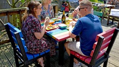 Four people enjoying an outdoor meal at a colourful garden table made from recycled plastic.