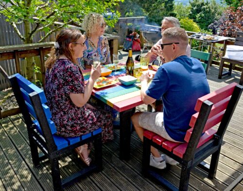Four people enjoying an outdoor meal at a colourful garden table made from recycled plastic.