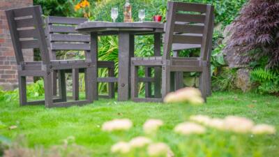 Recycled plastic dining set in a vibrant garden with a round table, four chairs, and a bottle of wine for an inviting outdoor setting