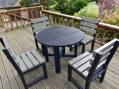 Black round garden table with matching black chairs made from recycled plastic.