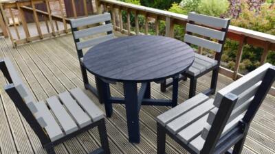 Black round garden table with matching black chairs made from recycled plastic.