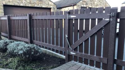 Brown fence made from artificial lumber in a residential garden with a garage in the background
