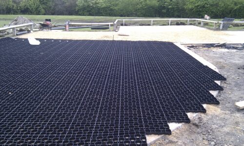 Permeable ground reinforcement grids being installed in a car park, with gravel and greenery in the background.