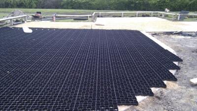 Permeable ground reinforcement grids being installed in a car park, with gravel and greenery in the background.