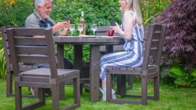 family of four dining outdoors at a brown recycled plastic table with brown chairs.