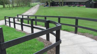Pathway with black recycled plastic handrails winding through green grass towards a building in a park setting
