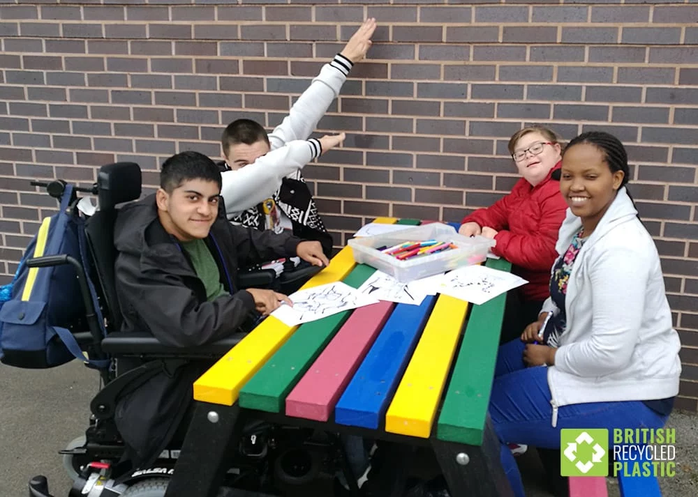 A group of four students sat outside around a multicoloured picnic table made from artificial lumber.