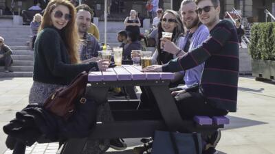 People enjoying a drink at a Denholme picnic table from British Recycled Plastic at the Piece Hall in Halifax, West Yorkshire.
