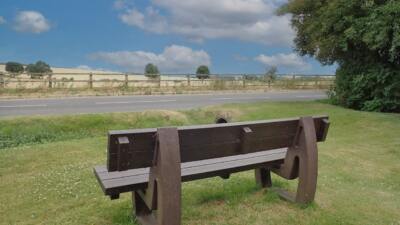 the rear view of a brown recycled plastic bench on some grass overlooking a road