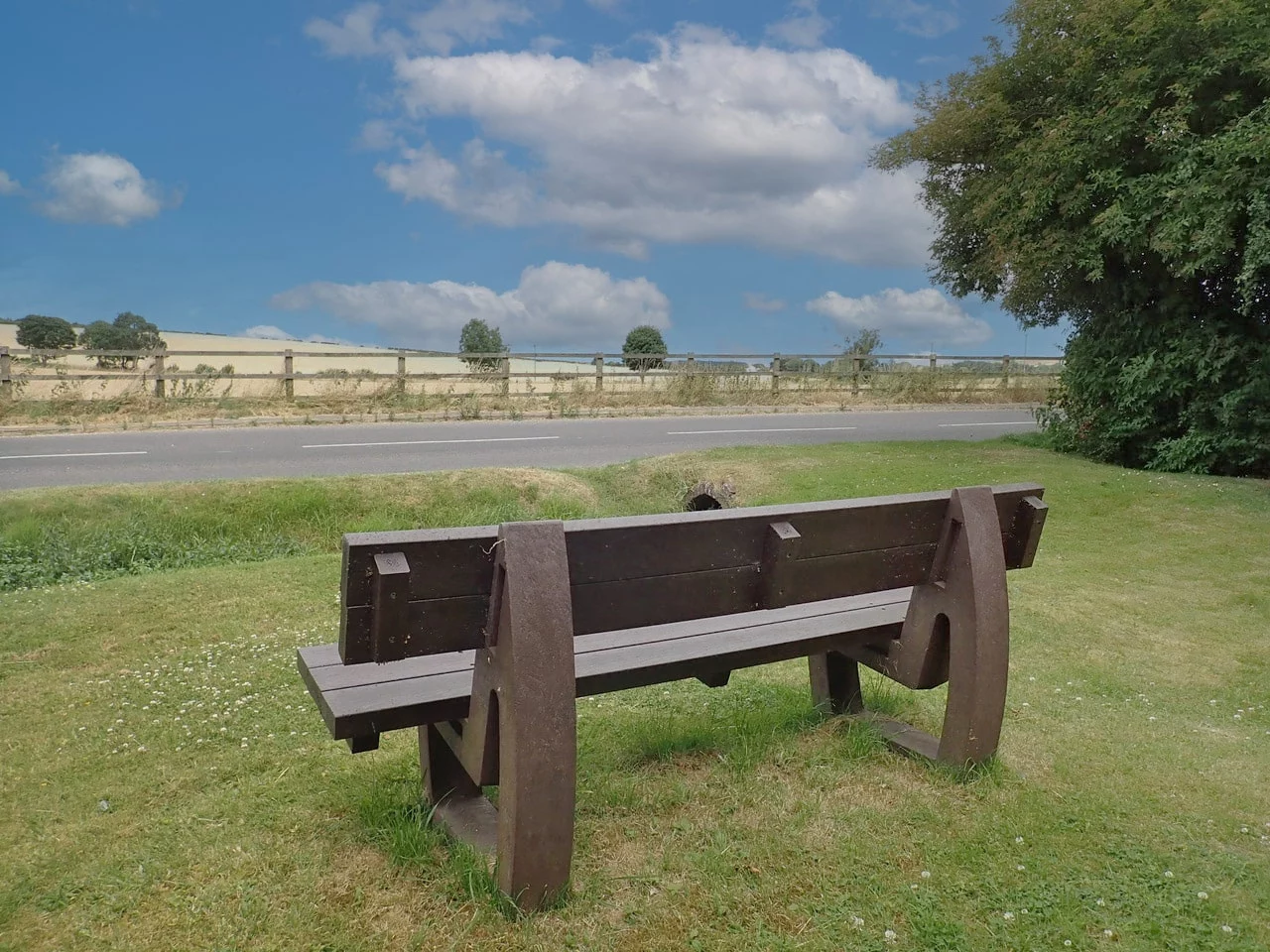 the rear view of a brown recycled plastic bench on some grass overlooking a road