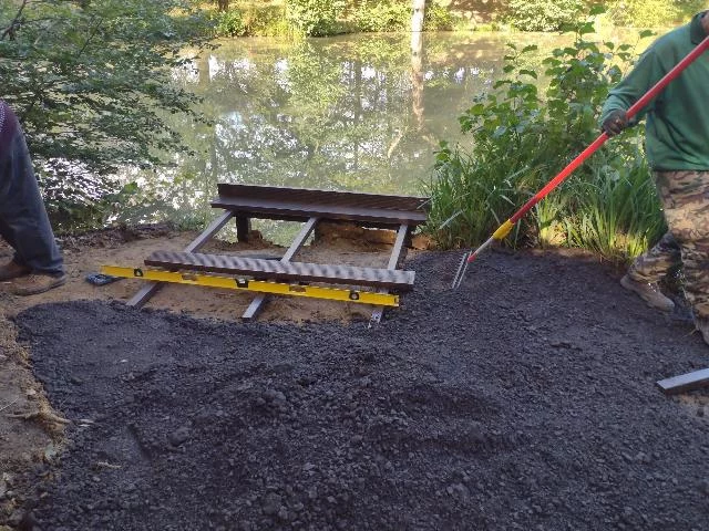 Construction of two fishing platforms on a small lake surrounded by lush green foliage.