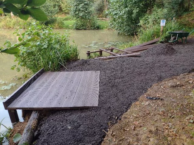 Construction of two fishing platforms on a small lake surrounded by lush green foliage.