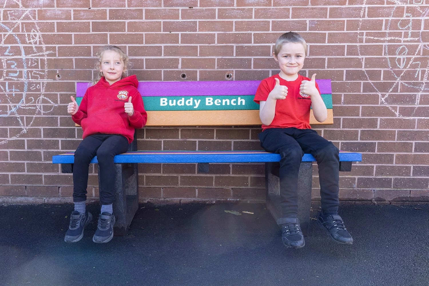 2 children smiling adn with thumbs up sitting on a british recycled plastic buddy bench
